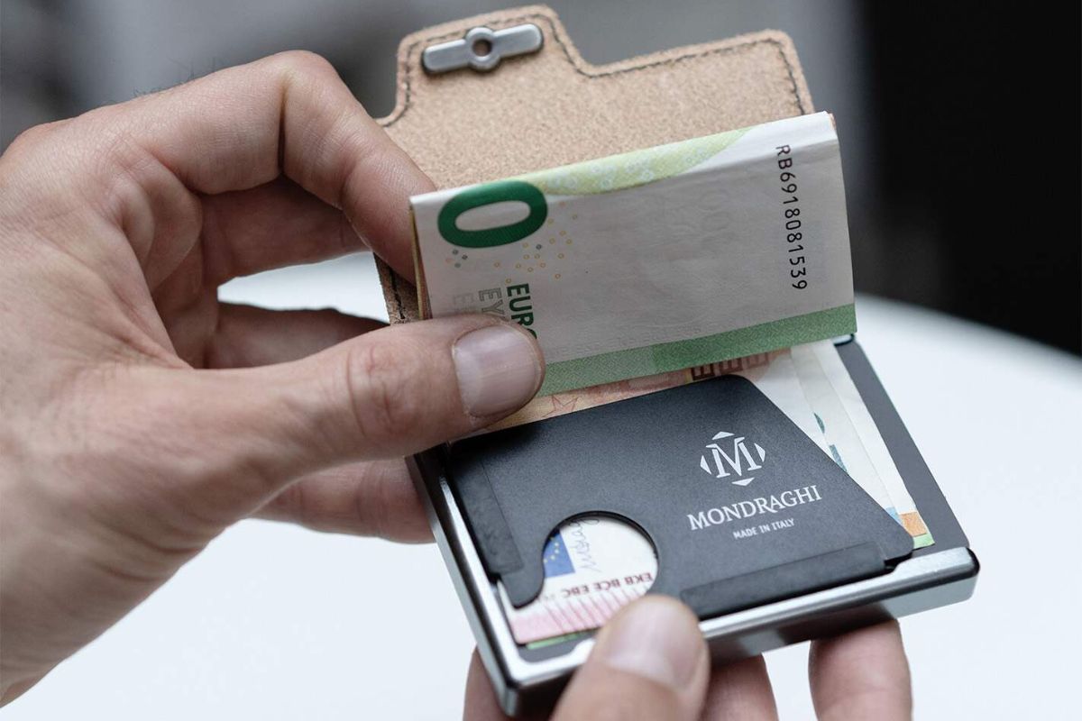A mini wallet open in a man’s hands, with the money clip clearly visible